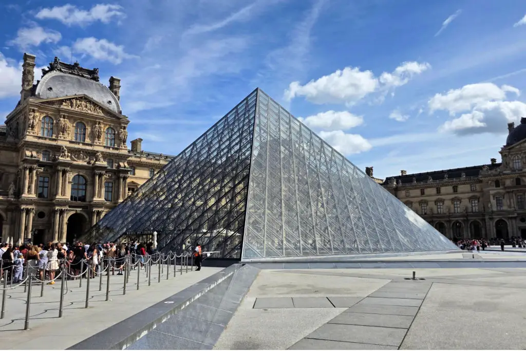 Modern glass pyramid entrance of the Louvre Museum contrasting with classical French palace architecture, Paris France